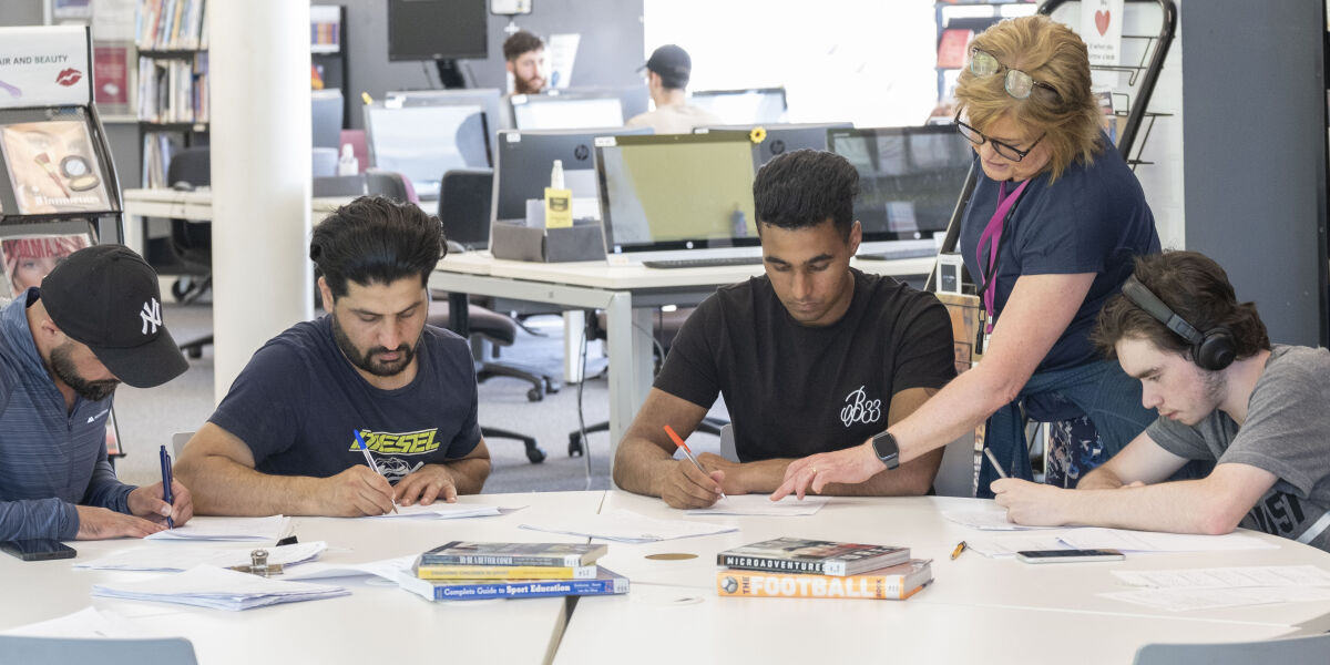 Lecturer talking to four male students at the library