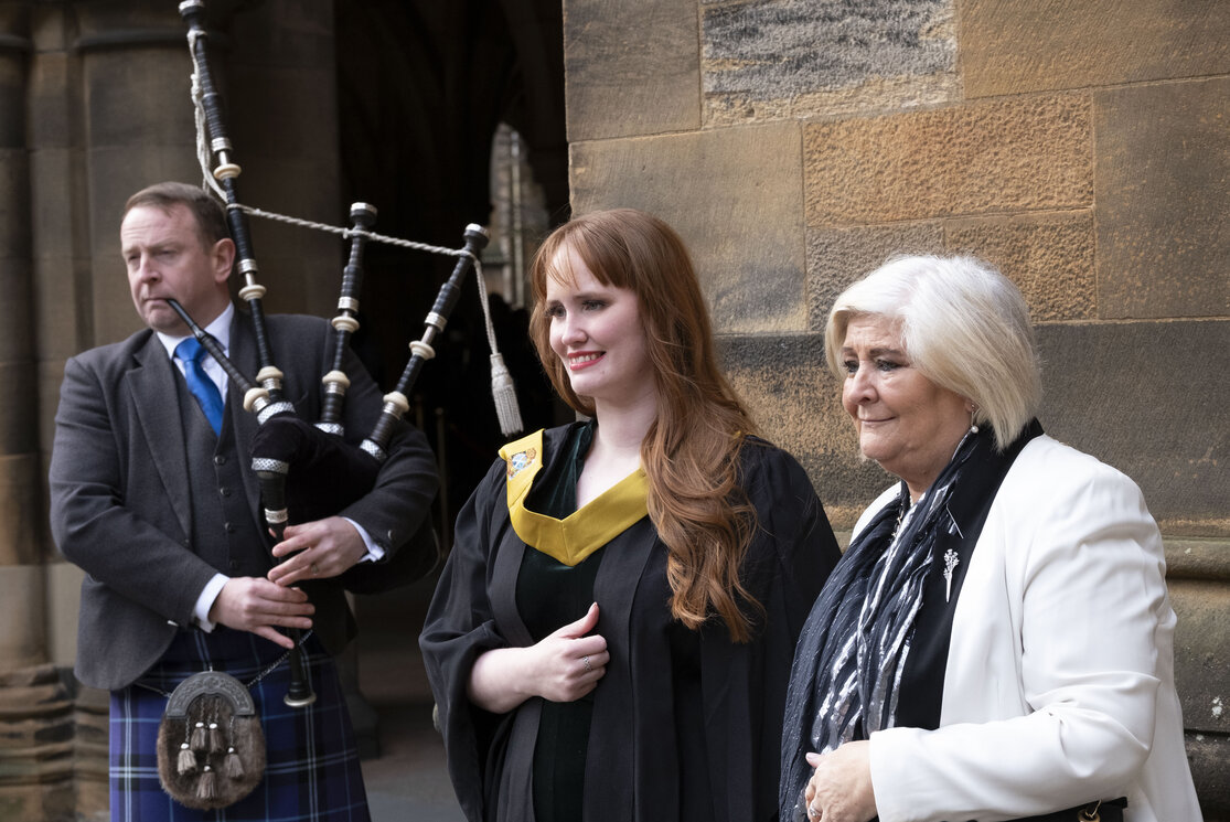 A female graduate with guest and piper in the background